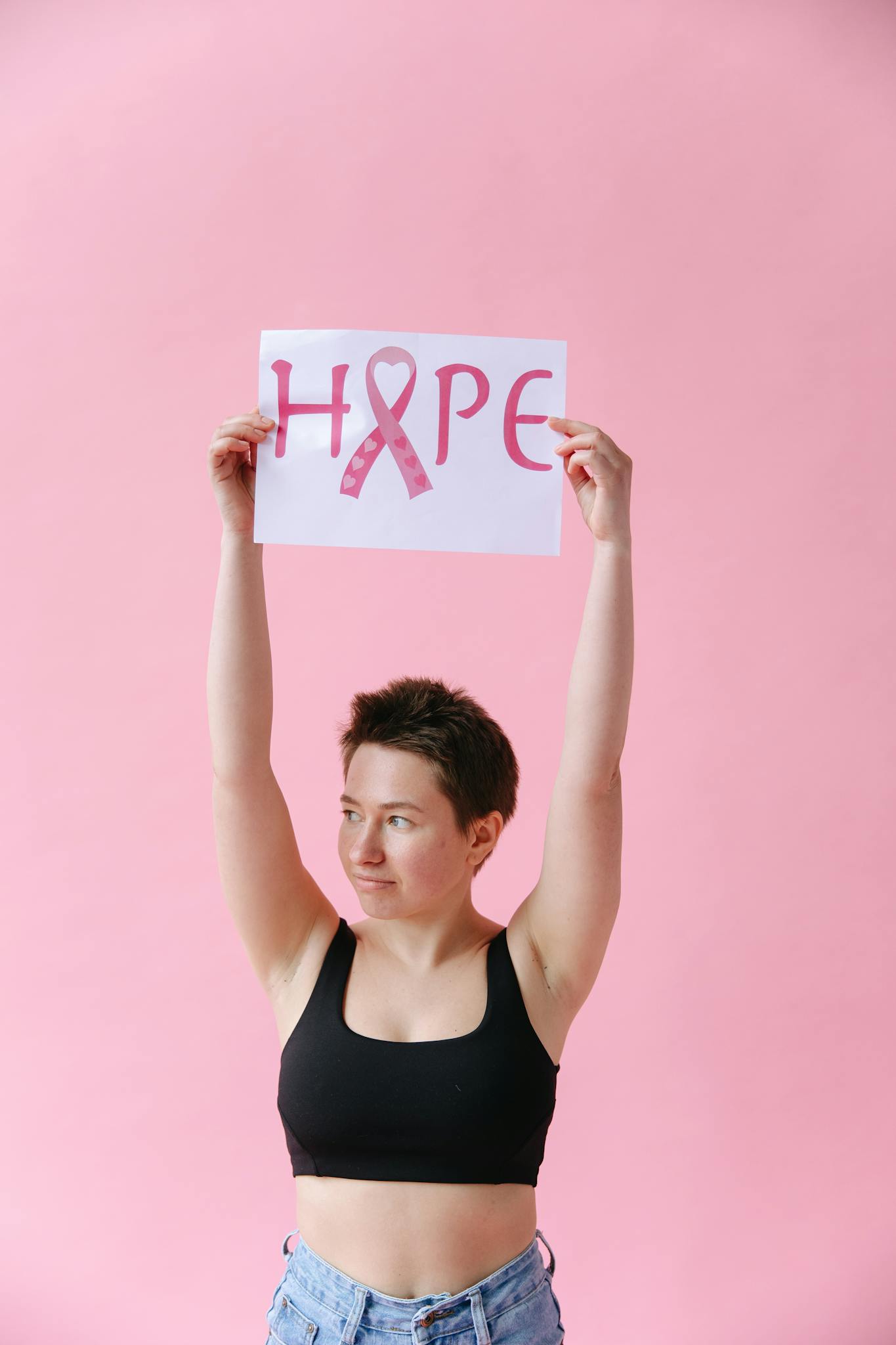 Woman holding 'Hope' sign for breast cancer awareness against pink background.